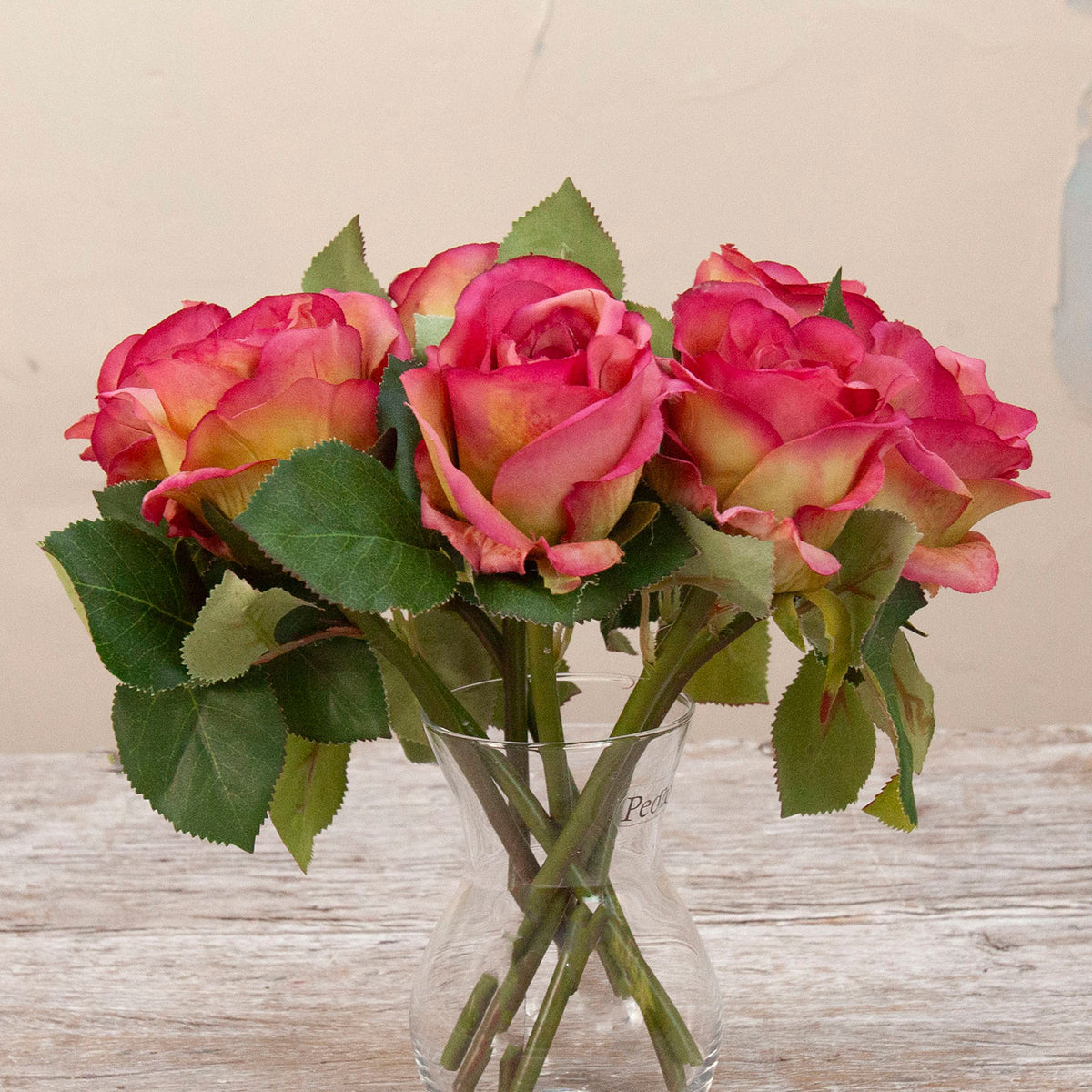 Close up of artificial pink rose stems with green foliage displayed in a clear glass vase
