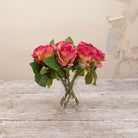 Artificial pink rose stems with green foliage displayed in a clear glass vase