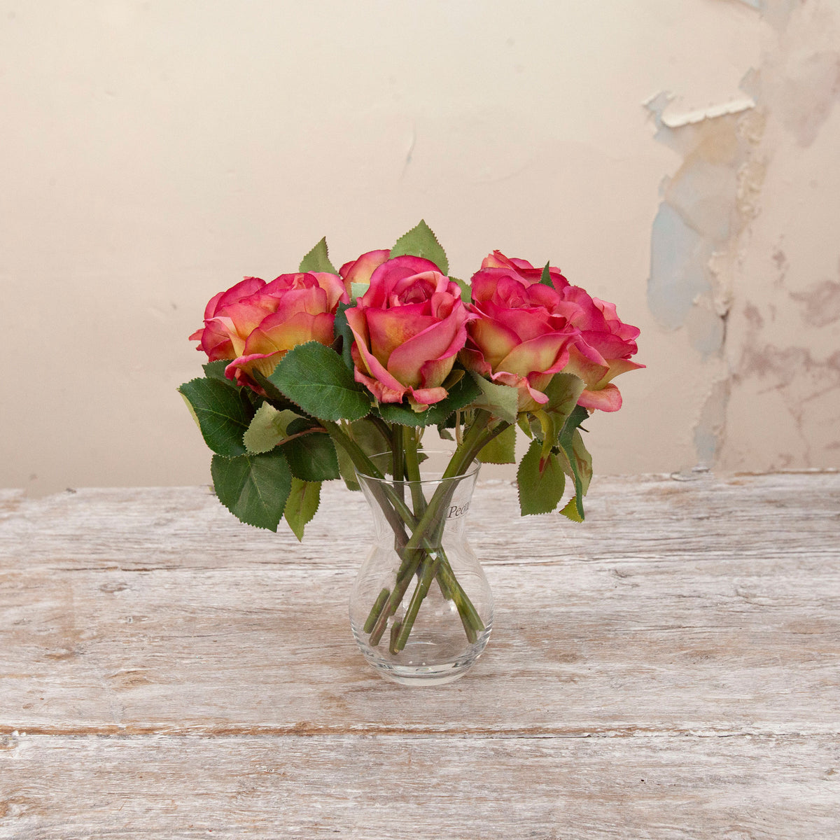Artificial pink rose stems with green foliage displayed in a clear glass vase