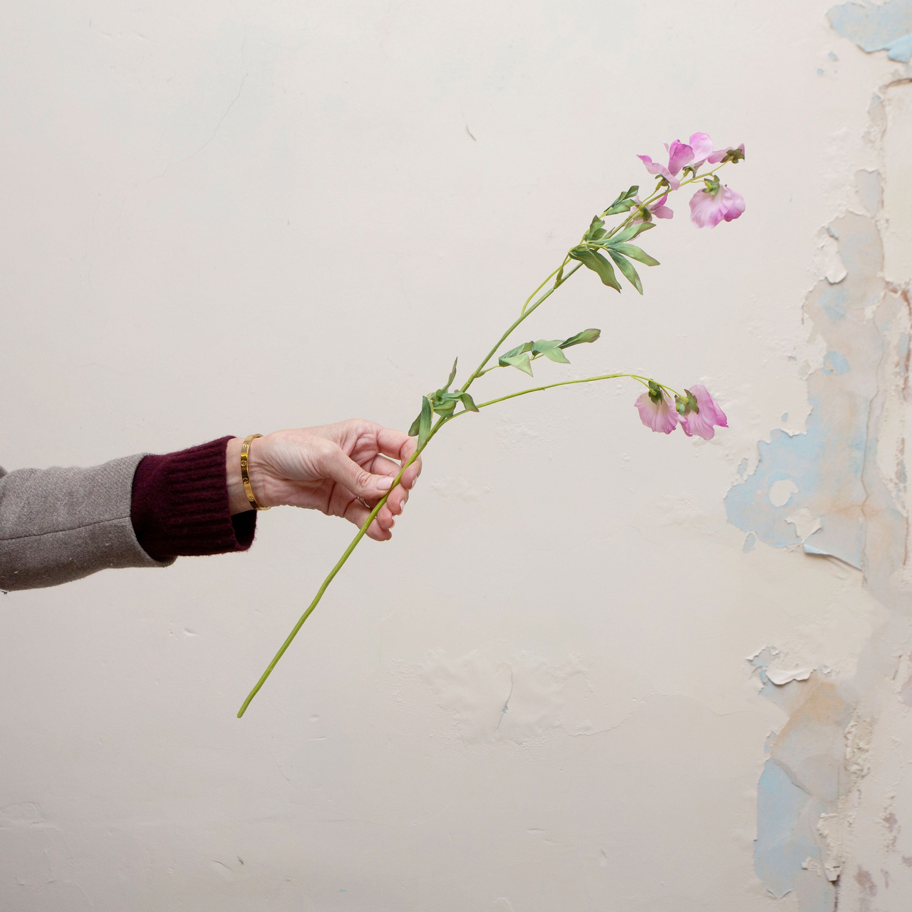 Artificial sweet pea stem being held in hand, featuring delicate purple-pink blooms with soft tonal variation on a slender green stem