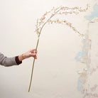 Artificial pale pink dancing orchid stem held in hand, featuring delicate orchid blooms on a gracefully arching stem.