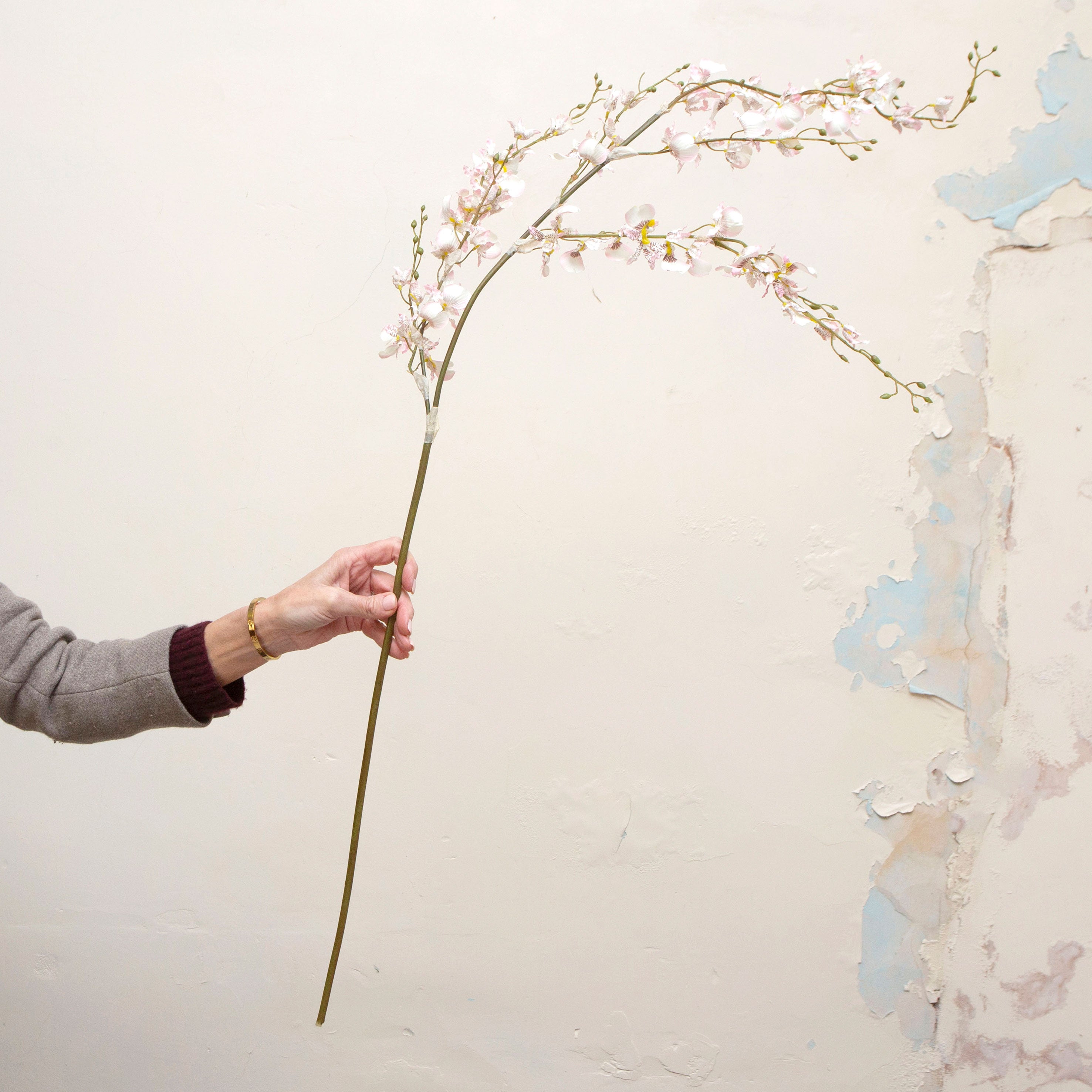 Artificial pale pink dancing orchid stem held in hand, featuring delicate orchid blooms on a gracefully arching stem.