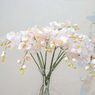 Close-up of artificial pale pink orchid flowers, showing soft blush-pink petals, warm yellow centres, gentle colour variation and natural veining.