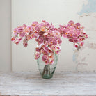 Artificial burgundy-pink speckled orchid stem displayed in a vase, showcasing cascading orchid flowers with blush-pink petals, fine speckling and realistic bud detail on a gently arching stem.