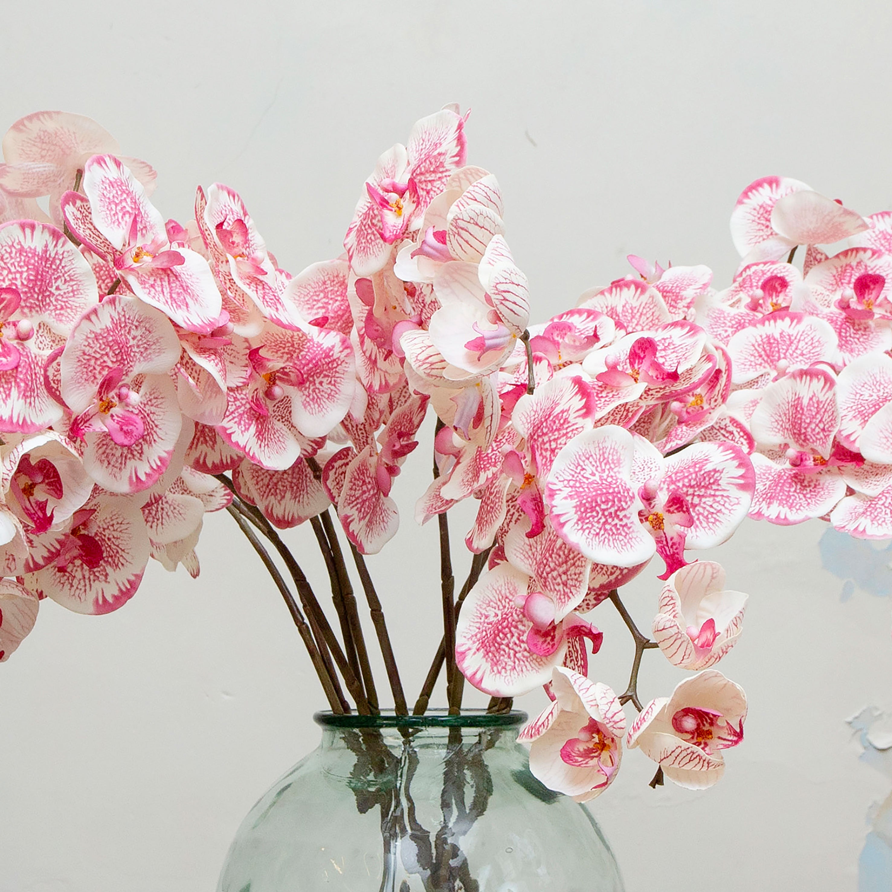 Close-up of artificial pink speckled orchid flowers, highlighting blush-white petals with vibrant pink speckling, warm yellow centres and lifelike texture and veining.”