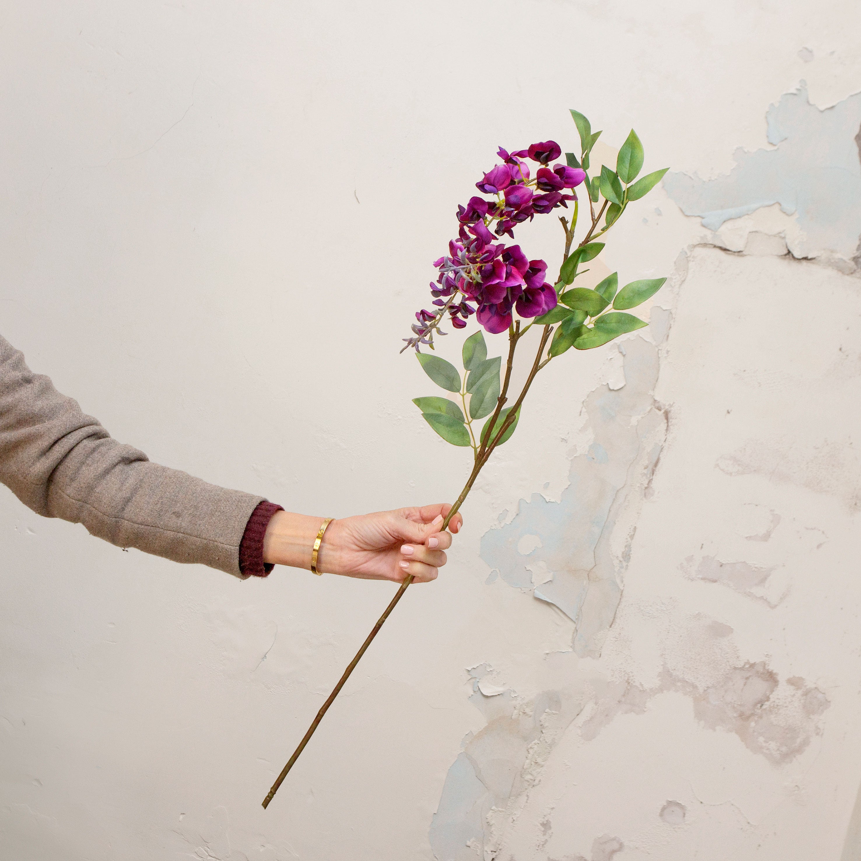 Artificial purple wisteria stem being held in hand, featuring cascading clusters of soft purple blooms with delicate petal detail on a natural-looking stem
