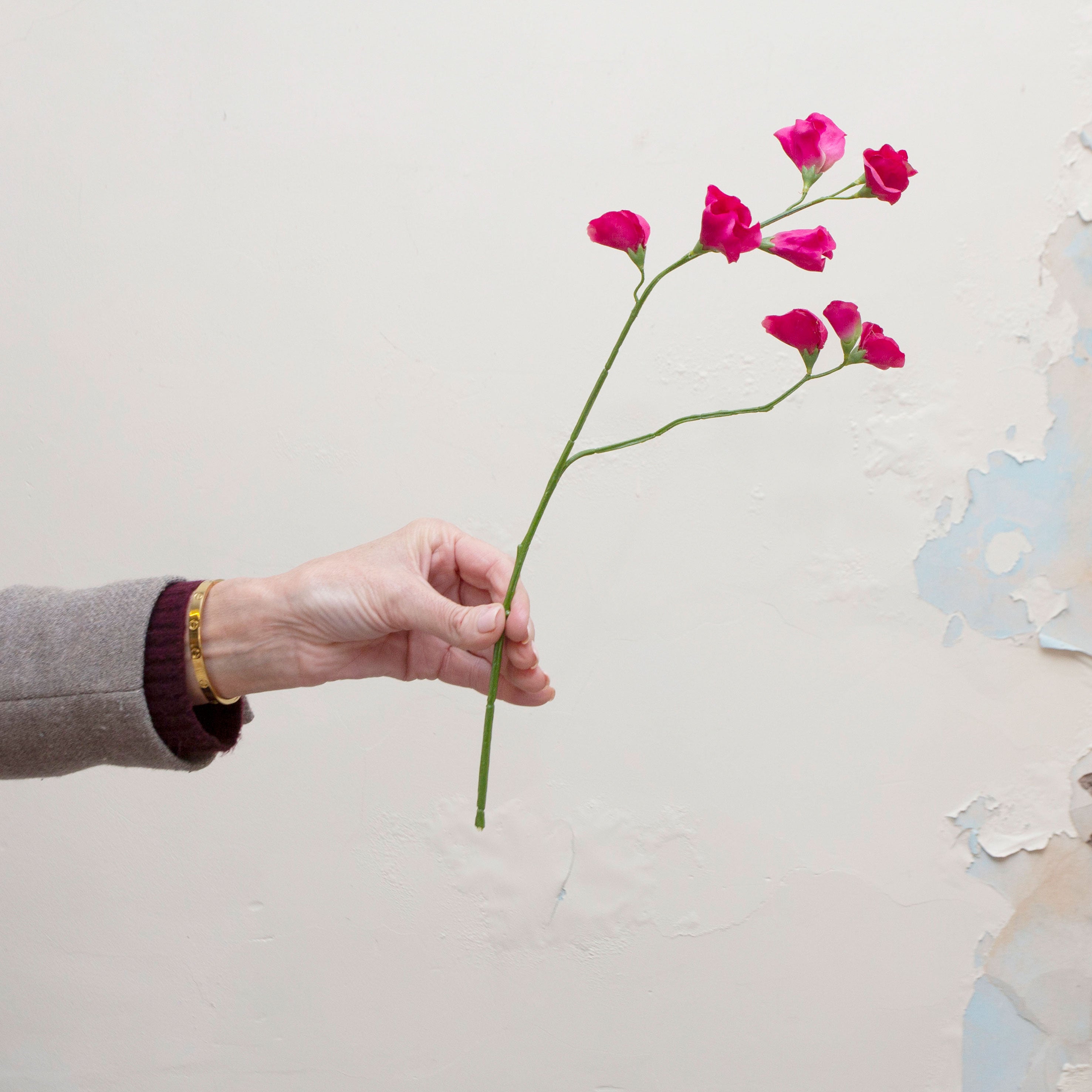 Artificial fuchsia sweet pea stem held in hand, featuring delicate fuchsia blooms on fine branching stems with green leaves.