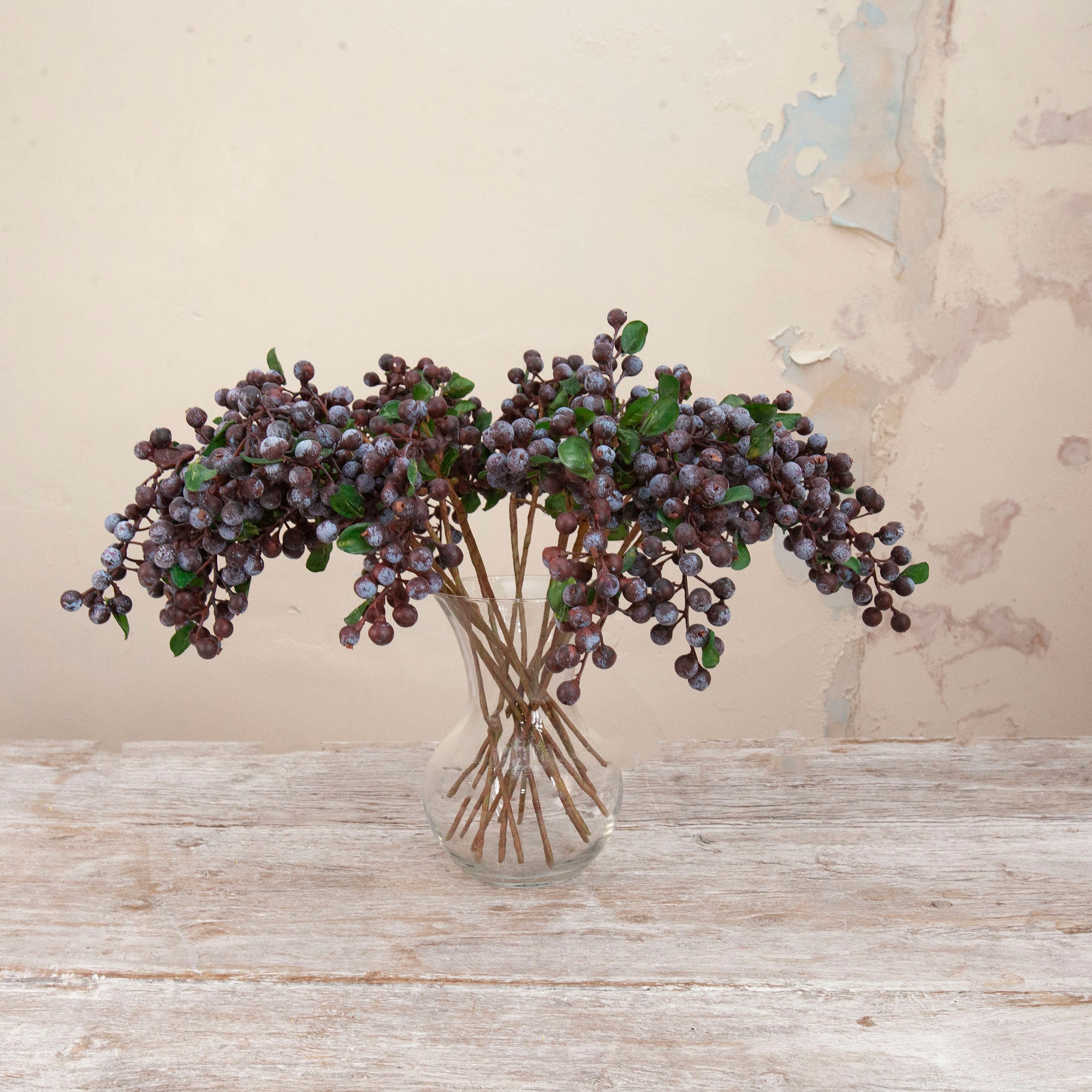 Artificial purple berry cluster stems with green foliage displayed in a clear glass vase