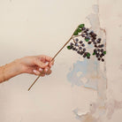 Hand holding artificial purple berry cluster stem with green foliage