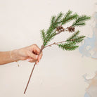 Hand holding artificial Pine Cone Stem with realistic green pine foliage and brown pine cones