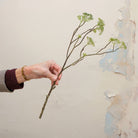 Artificial wild greenery foliage spray stem held in hand, featuring branching stems and fine green foliage.