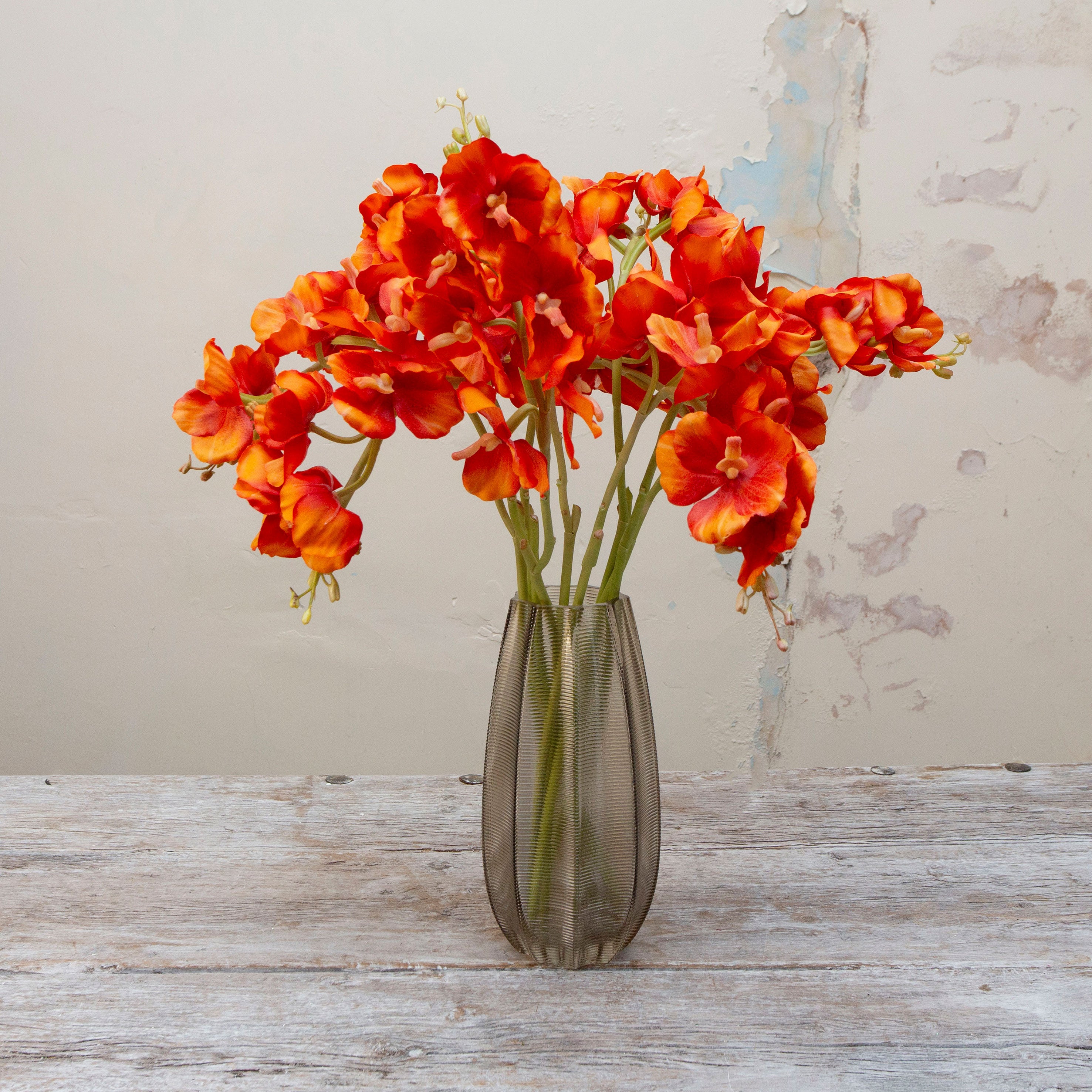 Artificial orange vanda orchid spray stems displayed together in a smoked glass vase for styling purposes