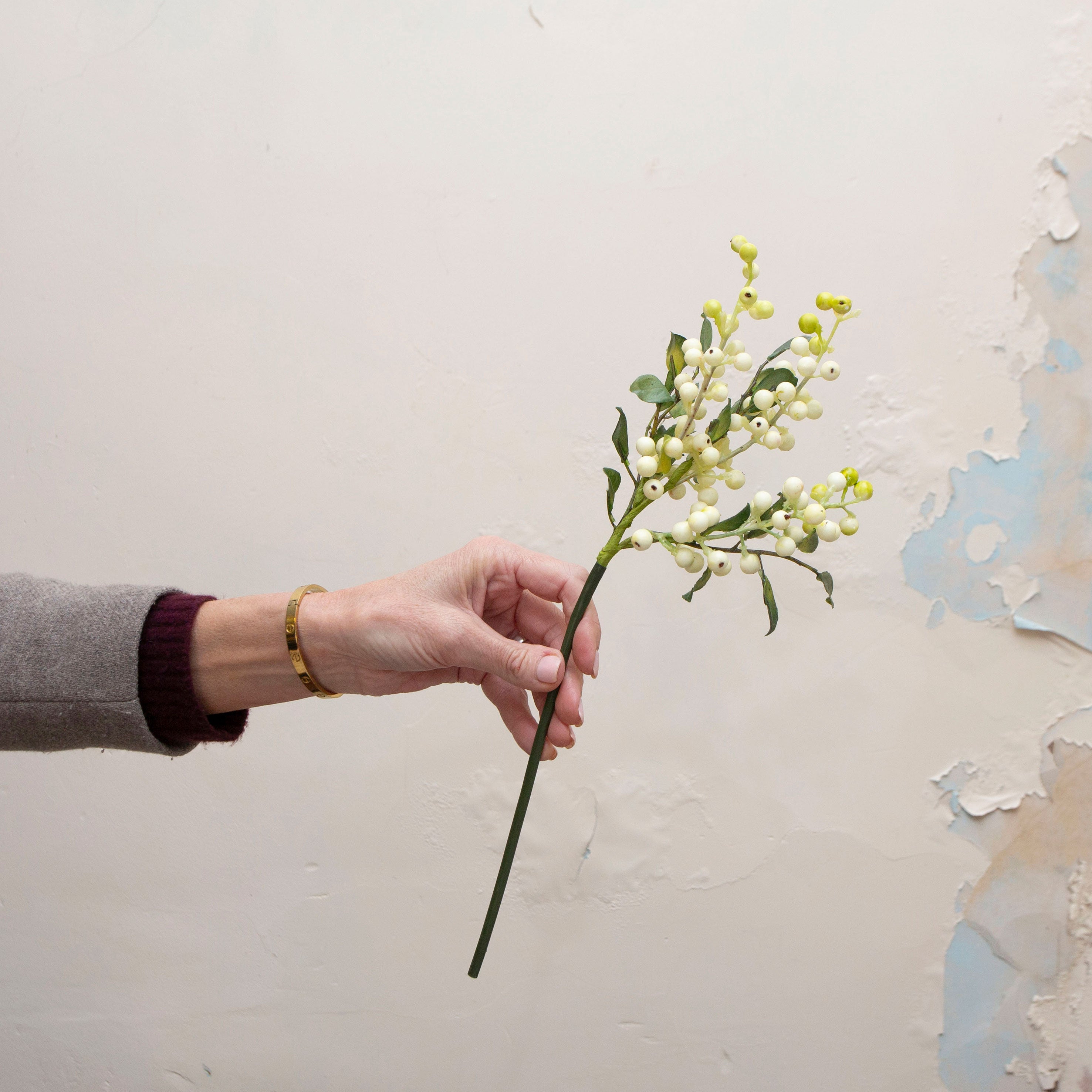 Artificial white and soft green berry stem being held in hand, featuring clusters of small round berries in creamy white and fresh green tones, with natural-looking foliage