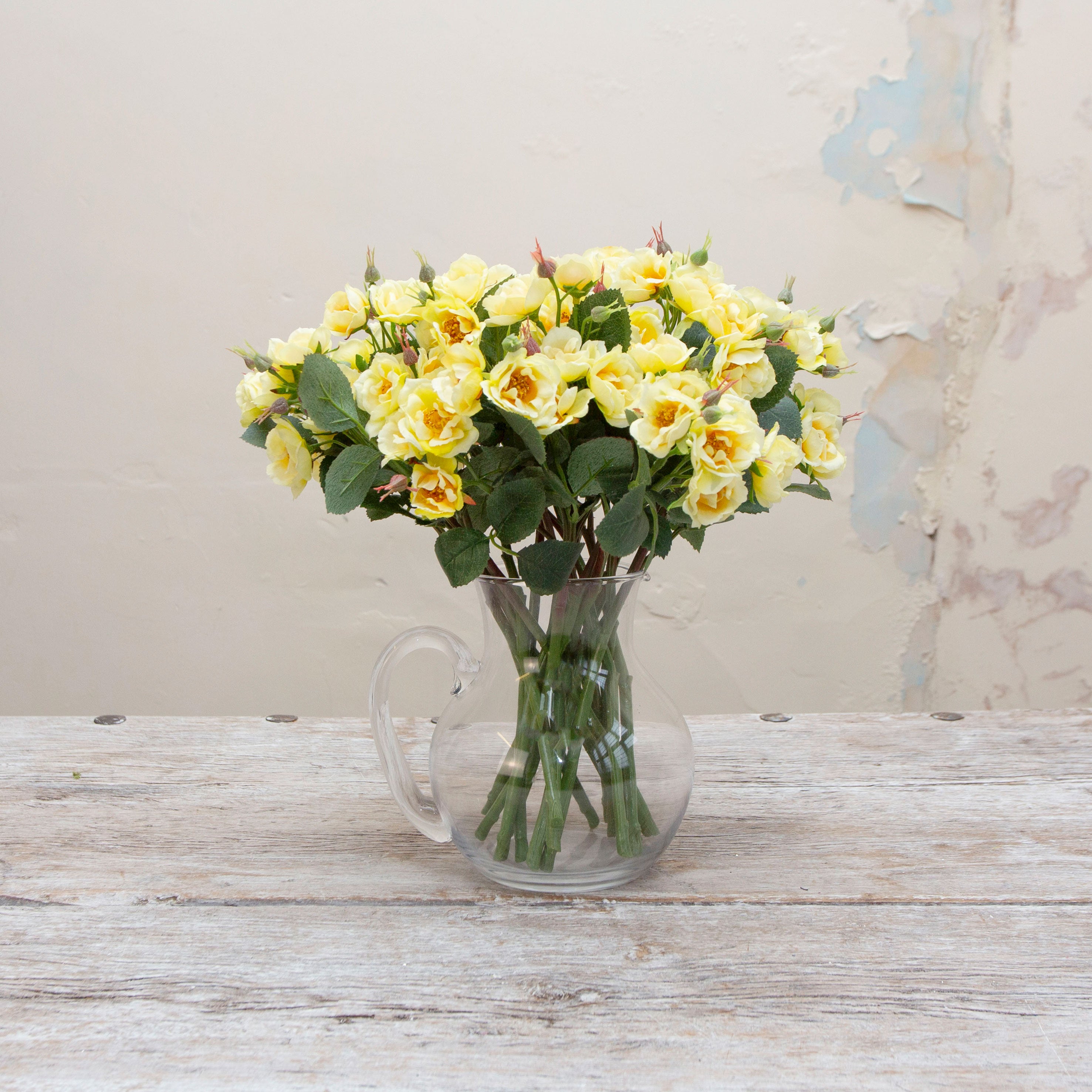 Artificial pale yellow rose spray stem displayed in a vase, showcasing softly opened roses, layered petals and natural green leaves