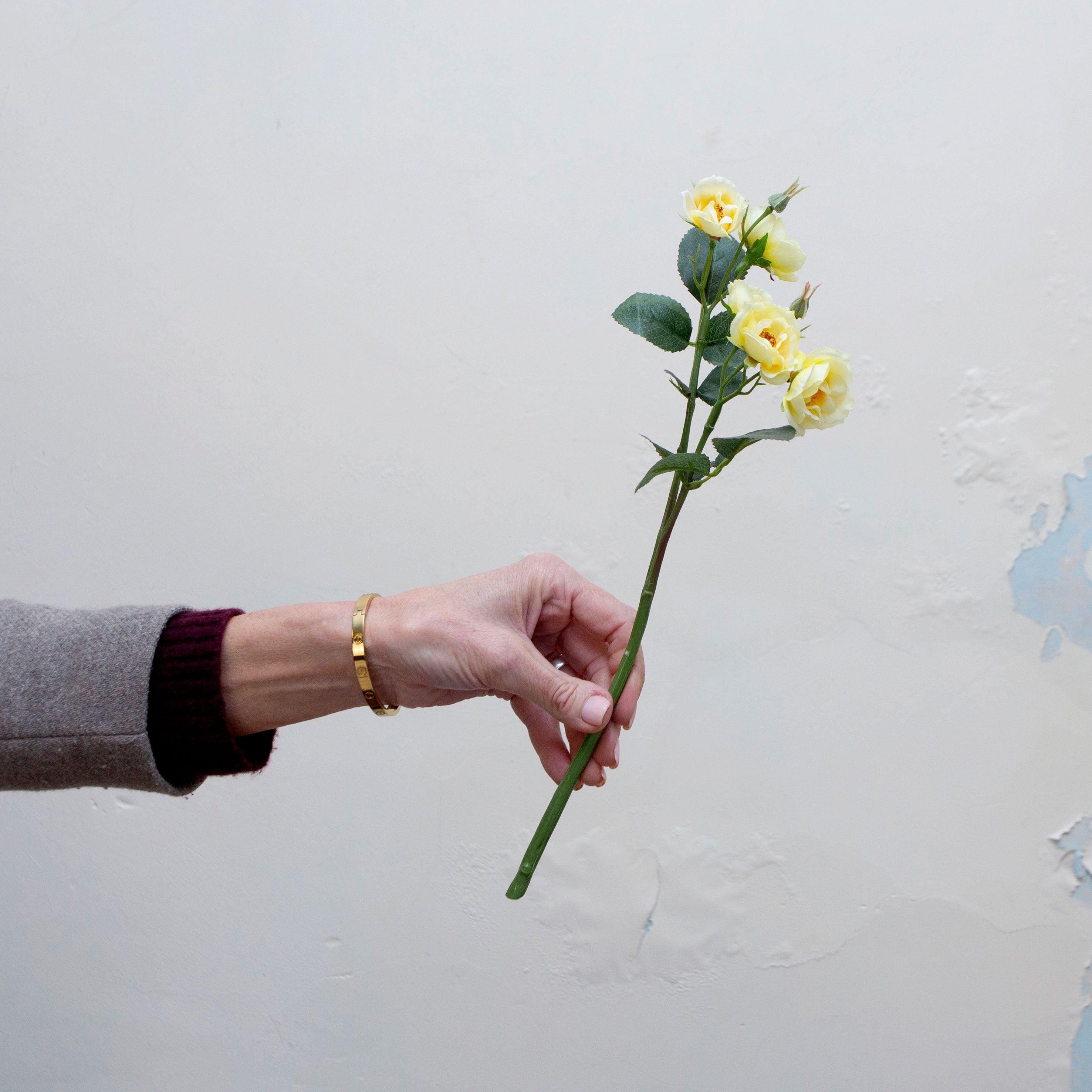 Artificial pale yellow rose spray stem being held in hand, featuring multiple open rose blooms and buds with realistic foliage on a natural-look stem