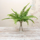 Artificial green fern spray stems displayed together in a clear glass vase for styling purposes.
