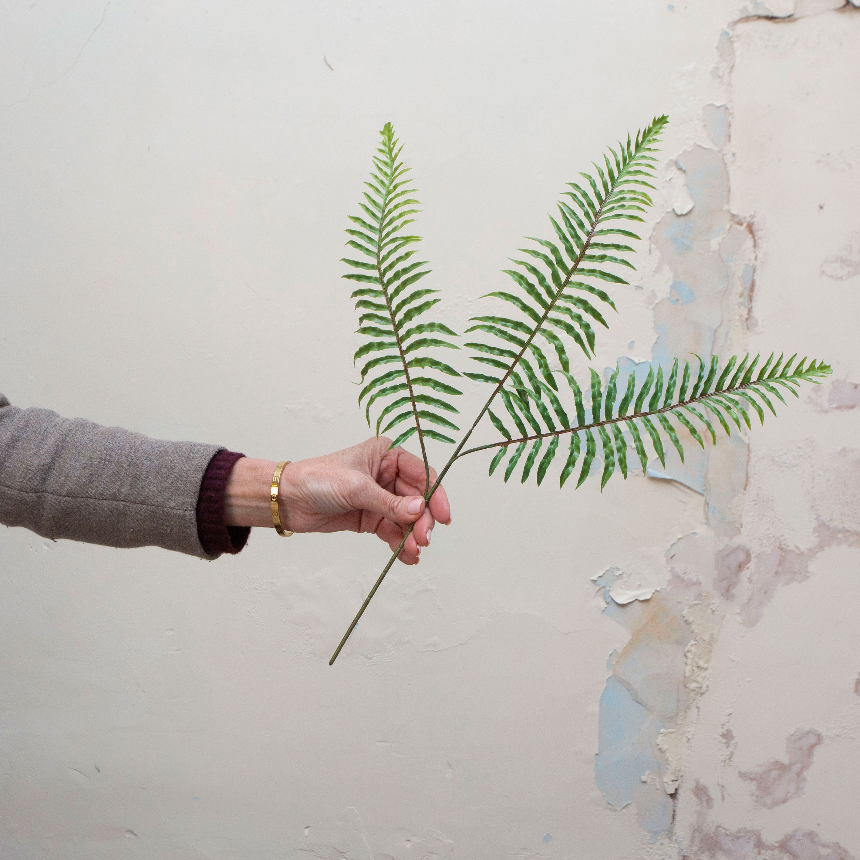 Artificial green fern spray stem held in hand, featuring long arching fronds and fine foliage