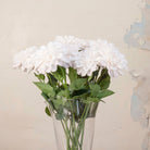 Close up of artificial White Dahlia Stems with full white blooms and realistic green foliage displayed in a clear glass vase