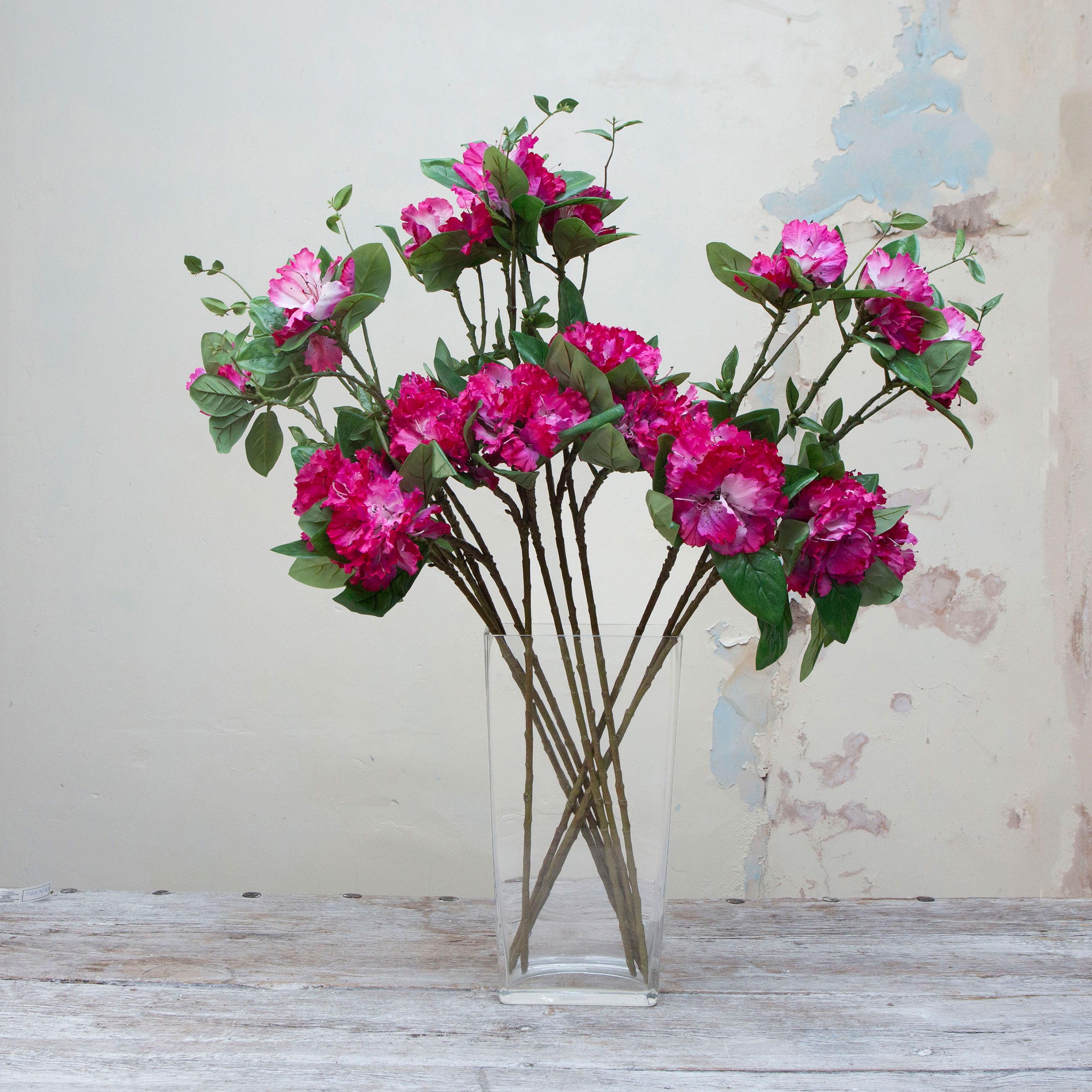 Artificial fuchsia pink rhododendron stems displayed together in a vase for styling purposes