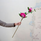 Artificial fuchsia pink rhododendron stem held in hand, featuring soft clustered blooms and green leaves on a woody stem