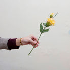 Artificial yellow lisianthus pick held in hand, featuring open blooms and buds with soft peach edging and green foliage