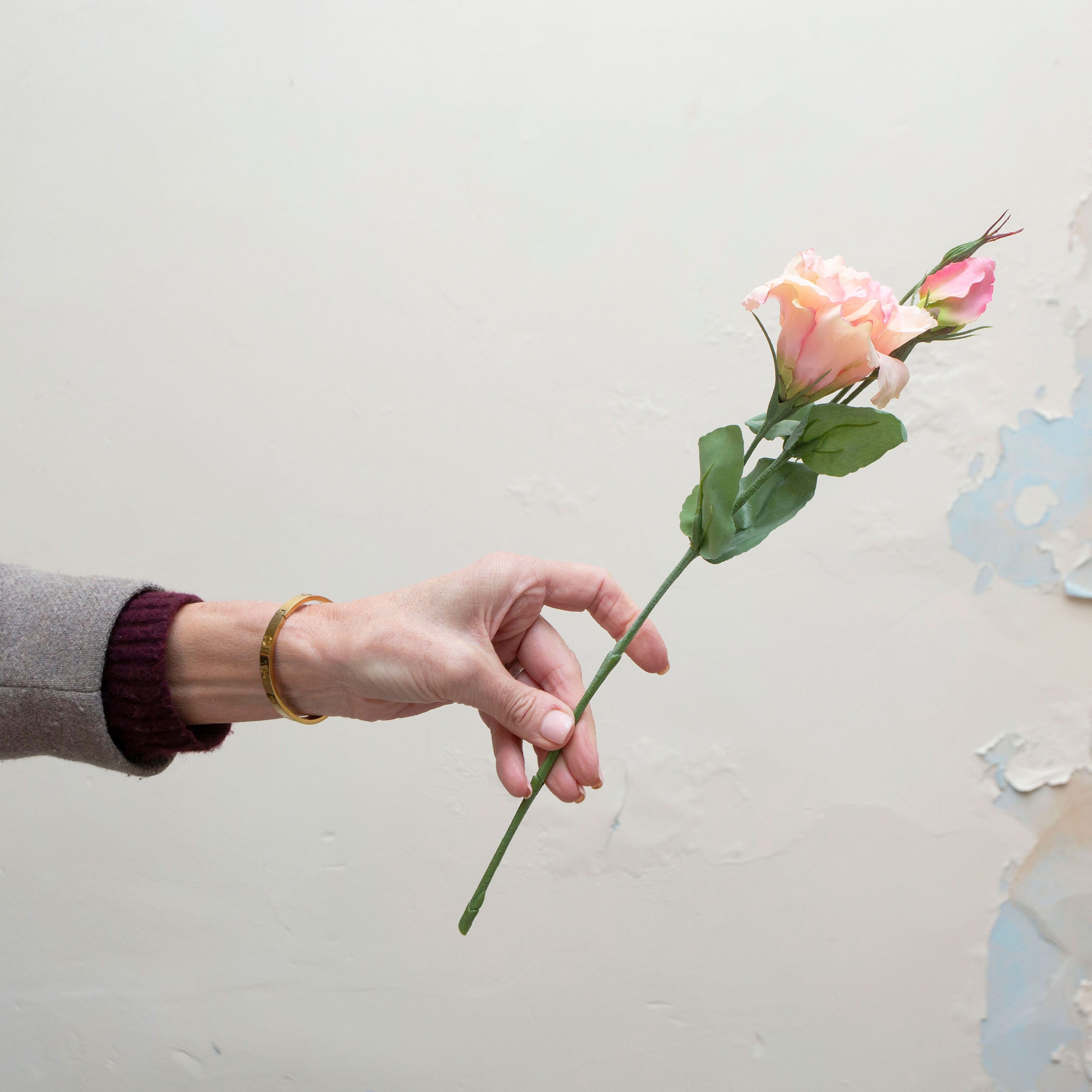 Artificial soft peach blush lisianthus pick held in hand, featuring gently layered blooms and realistic green foliage