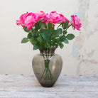 Artificial pink rose stems displayed together in a smoked glass vase for styling purposes.