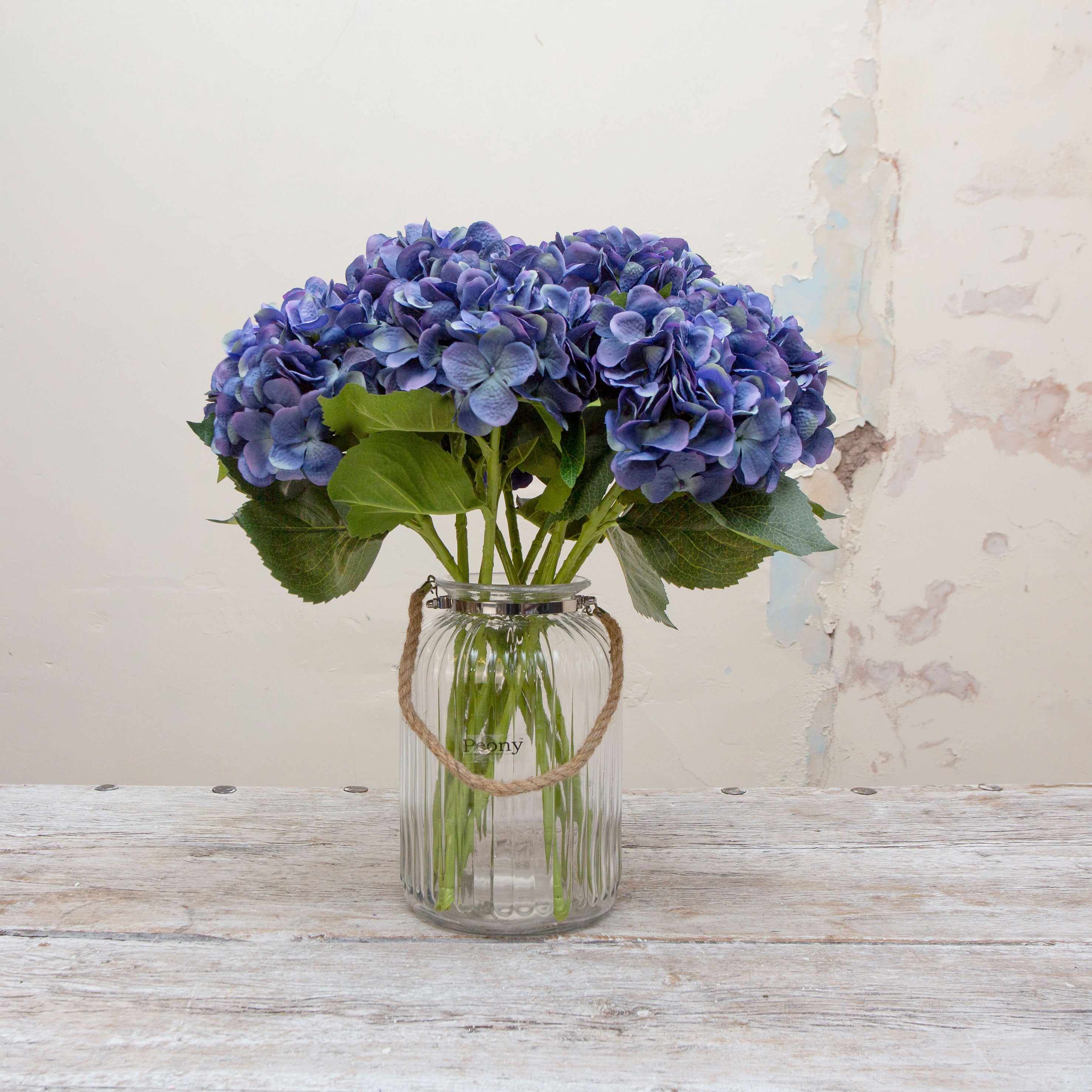 Artificial deep blue hydrangea stems displayed together in a vase for styling purposes.