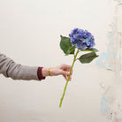Artificial deep blue hydrangea stem held in hand, featuring dense clustered blooms and rich blue tones
