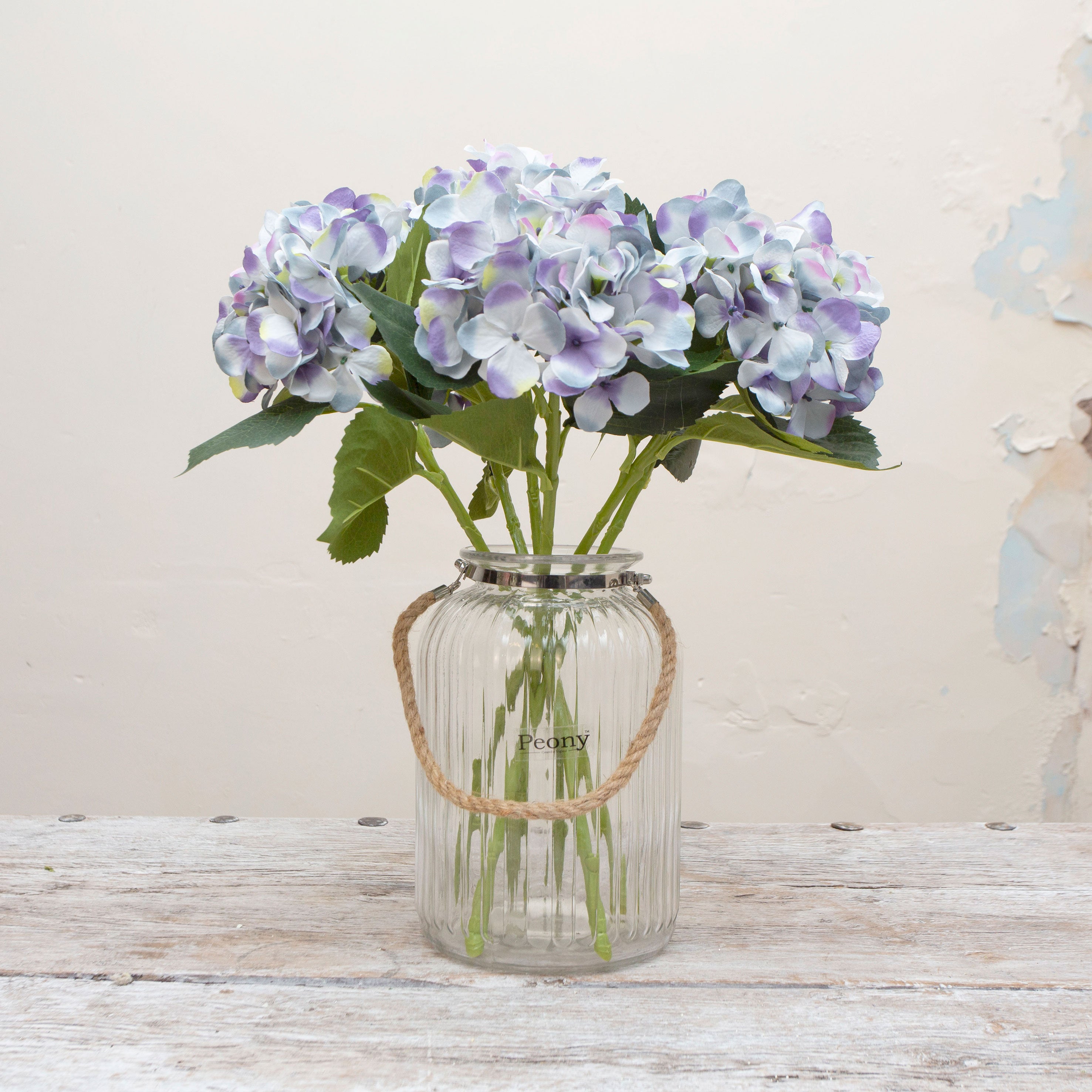 Artificial soft blue lilac hydrangea stems displayed together in a vase for styling purposes.