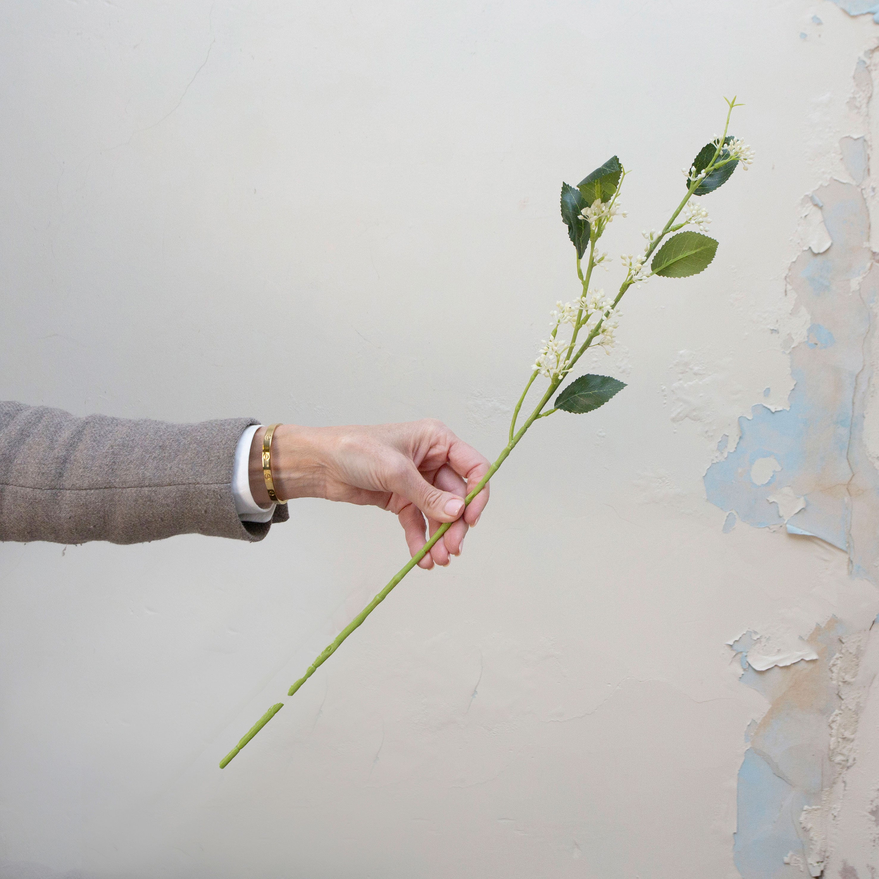 Artificial bridal white wild berry stem held in hand, featuring small clustered berry buds on a slender green stem with leaves