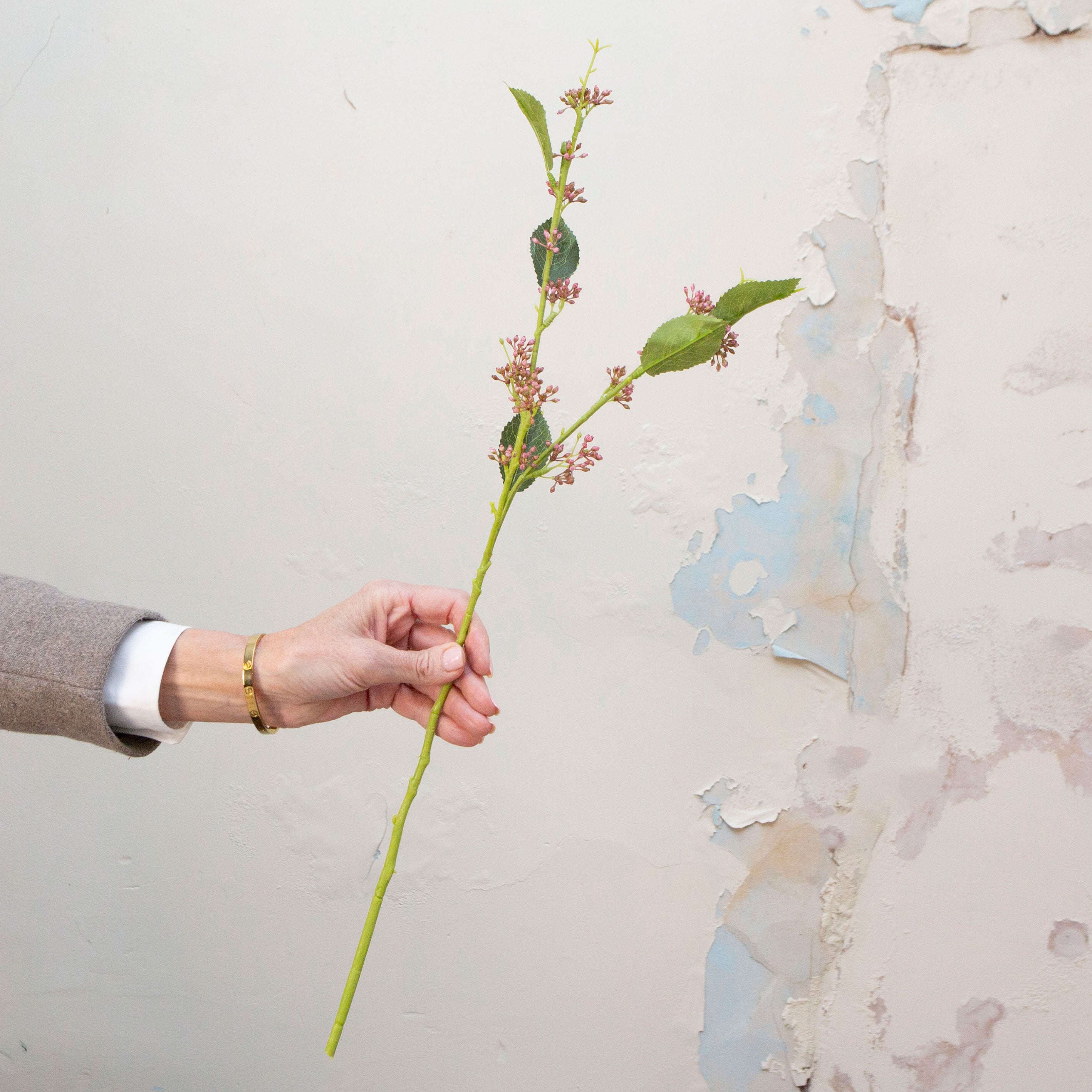Artificial mauve-pink wild berry stem held in hand, featuring small clustered berry buds on a slender green stem with leaves