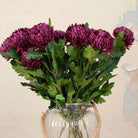 Close up of Artificial Chrysanthemum Stems with rich burgundy blooms and realistic green foliage displayed in a clear ribbed glass vase