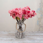 Artificial pink cherry blossom spray stems with layered blossoms, displayed together in a glass vase for display.