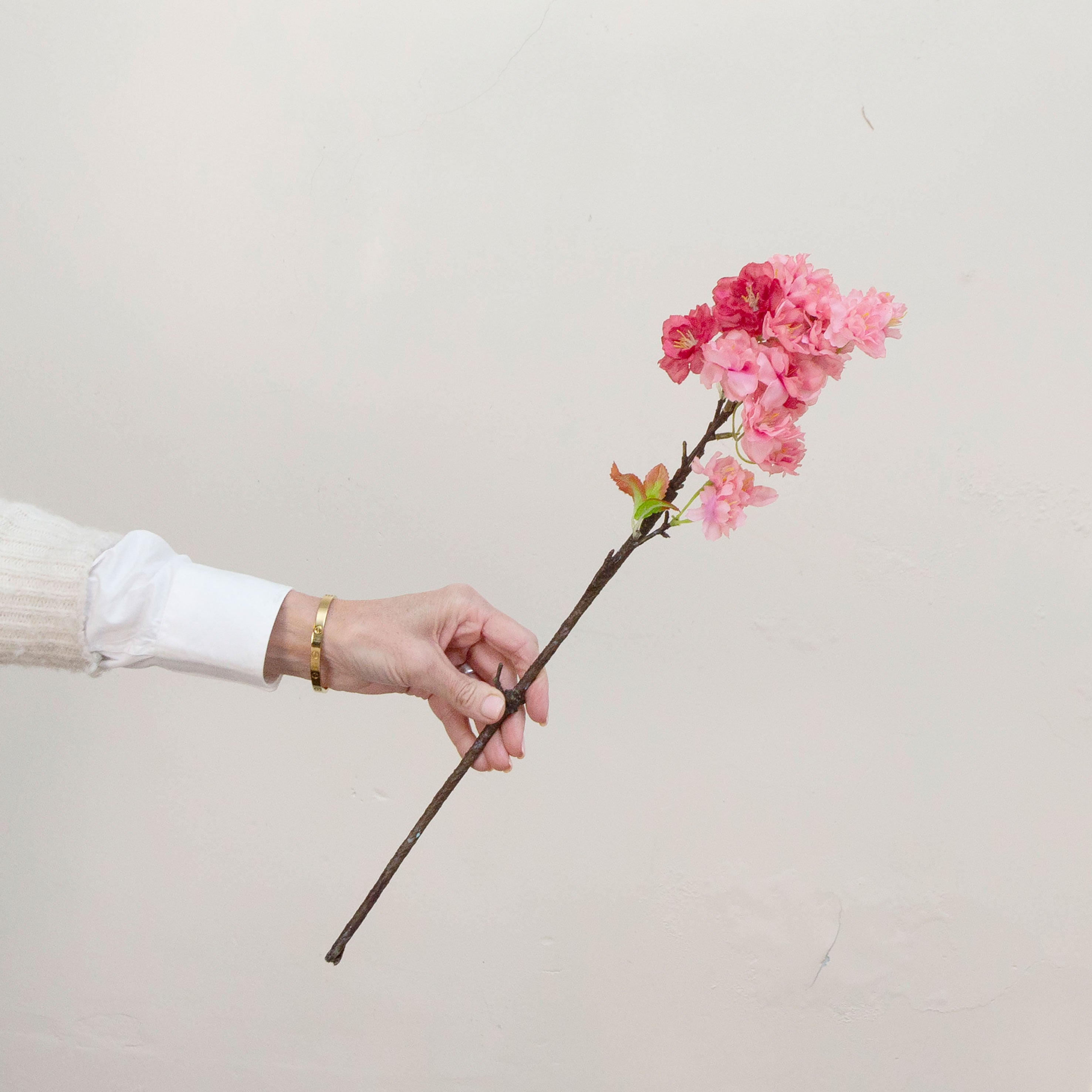 Artificial pink cherry blossom stem held in hand, featuring clustered blossoms and natural branching.