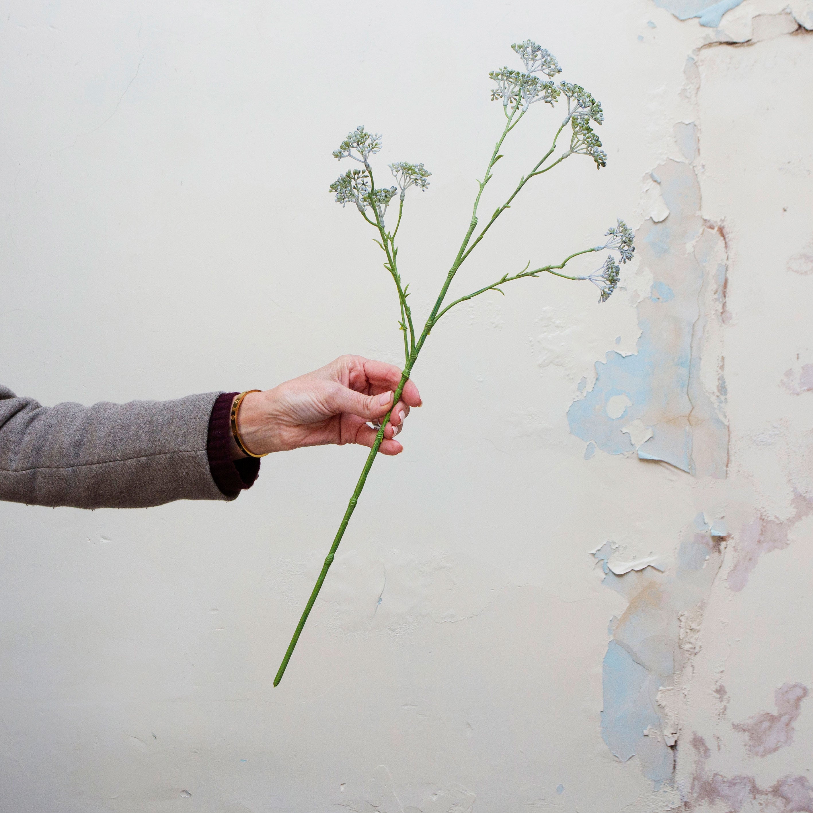 Artificial soft pale blue patrinia spray stem held in hand, featuring delicate clustered flowers on fine branching stems