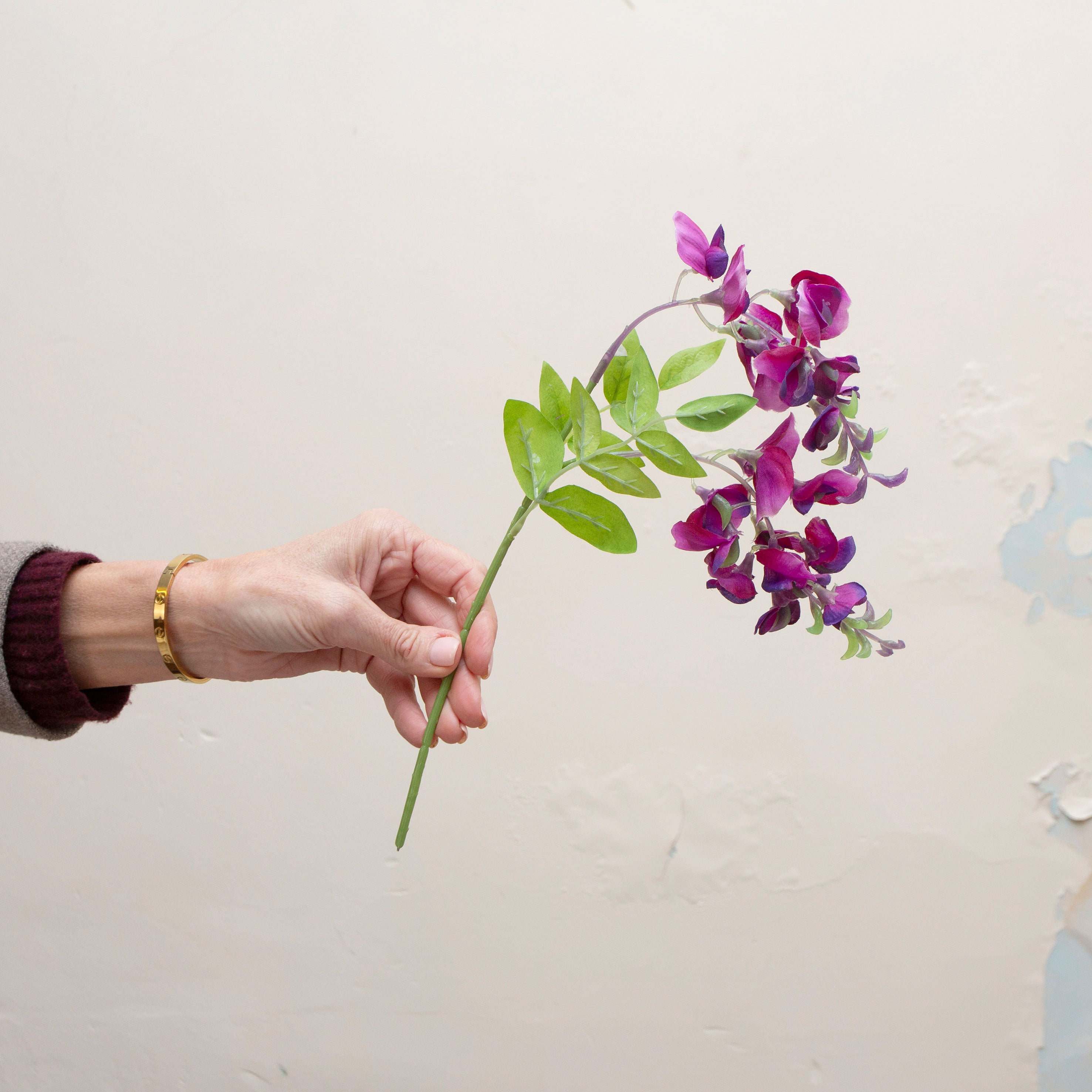 Artificial purple sweet pea stem held in hand, featuring delicate purple blooms and fresh green leaves.