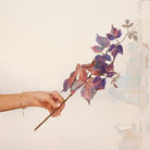 Hand holding Artificial Leaf Foliage Stem with trailing purple, burgundy and muted autumn-toned leaves 