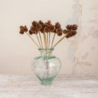 Artificial Pine Cone Stems with natural brown pine cones on long stems displayed in a clear green-tinted glass vase