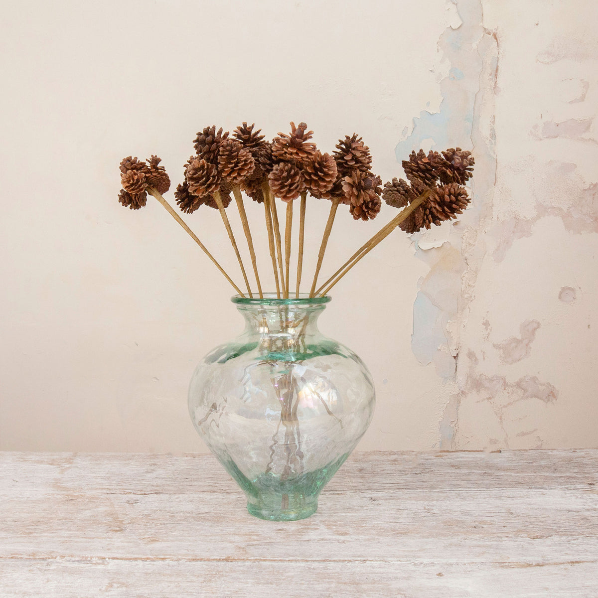 Artificial Pine Cone Stems with natural brown pine cones on long stems displayed in a clear green-tinted glass vase