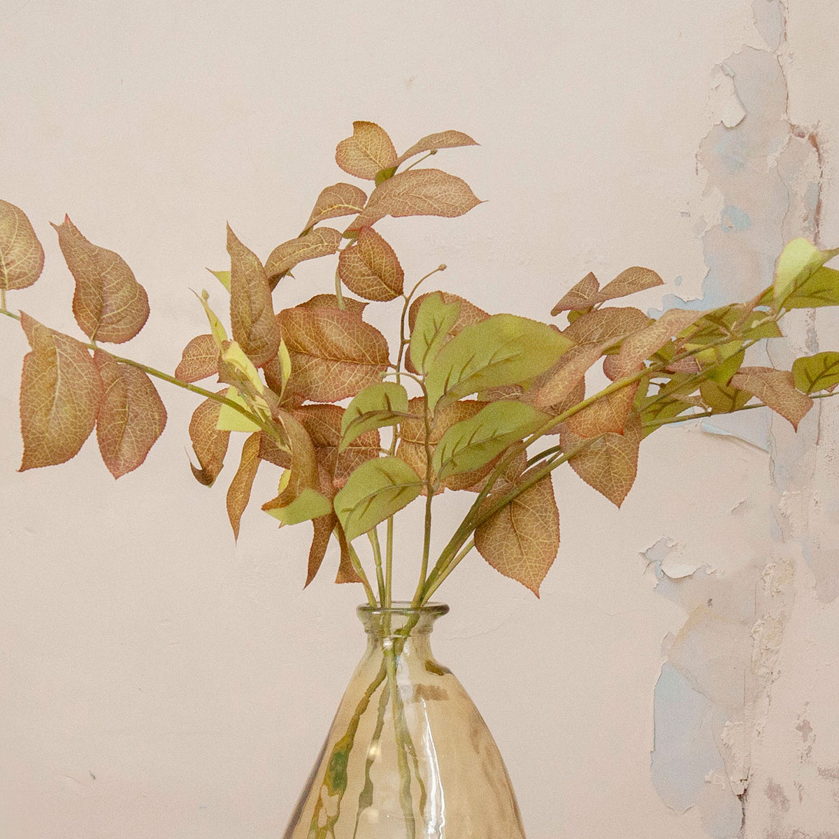 Close up of Artificial Salal Leaf Stems with green, bronze and warm brown foliage displayed in an amber-tinted glass vase
