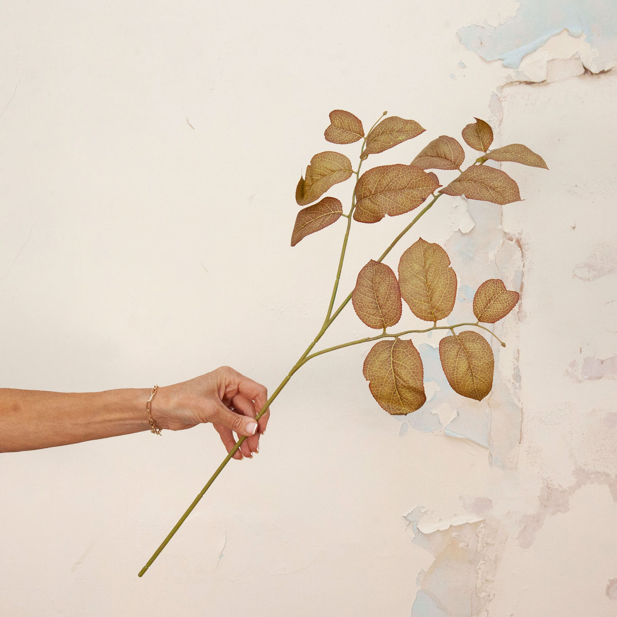 Hand holding Artificial Salal Leaf Stem with green, bronze and warm brown foliage 