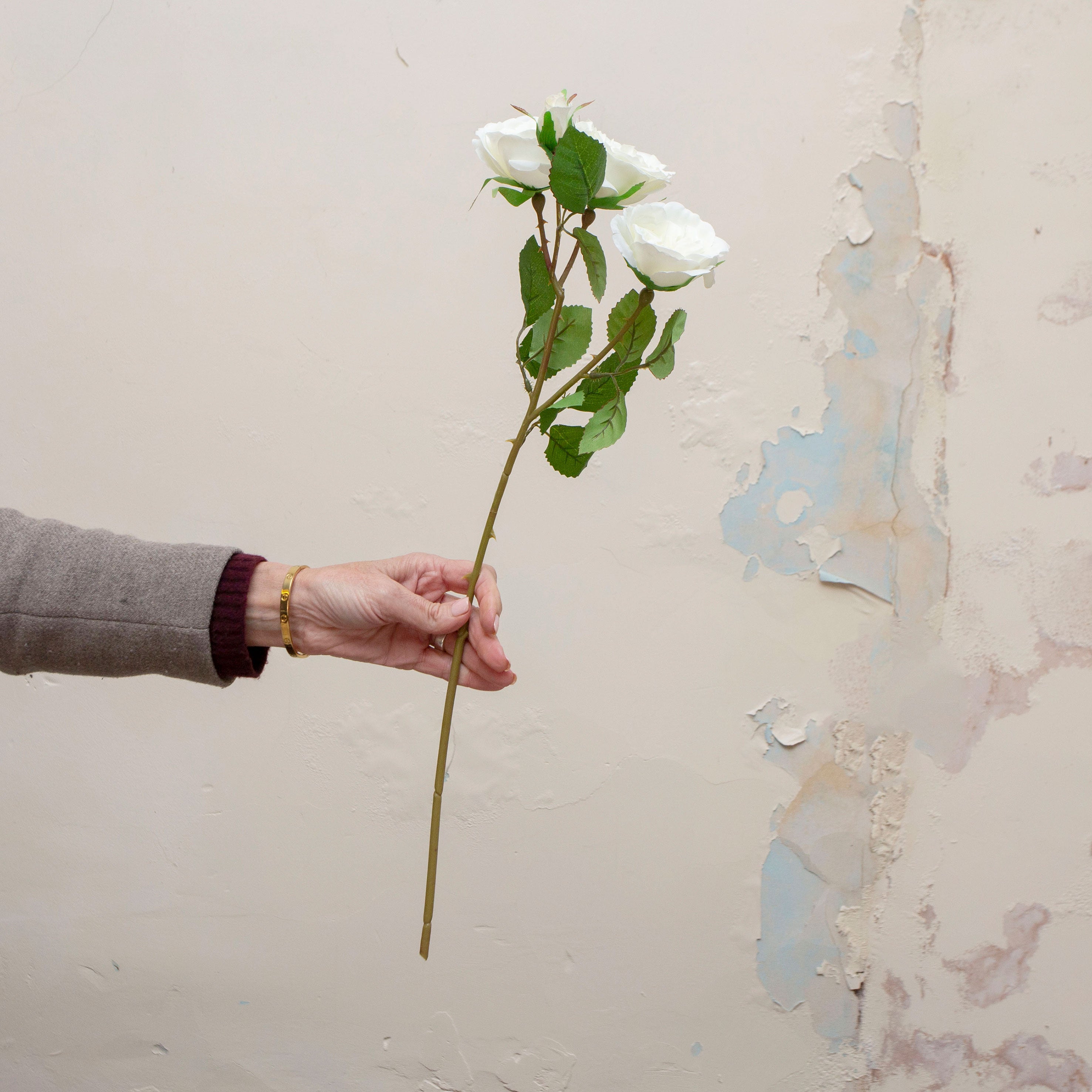 Artificial white rose spray stem held in hand, featuring multiple open rose blooms and realistic green foliage