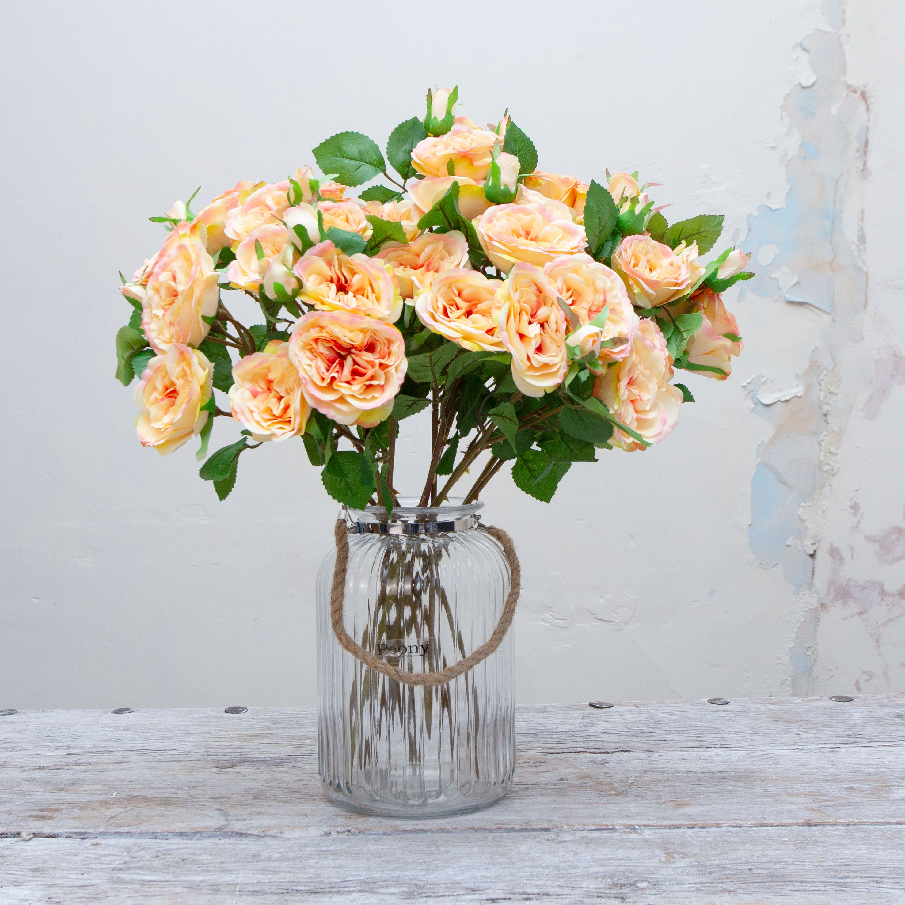 Artificial peach rose spray stems displayed together in a vase for styling purposes.