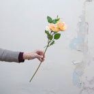 Artificial peach rose spray stem held in hand, featuring multiple open rose blooms and realistic green foliage