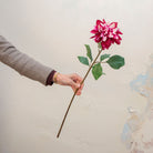 Hand holding an artificial magenta dahlia stem with some white petals mixed in.
