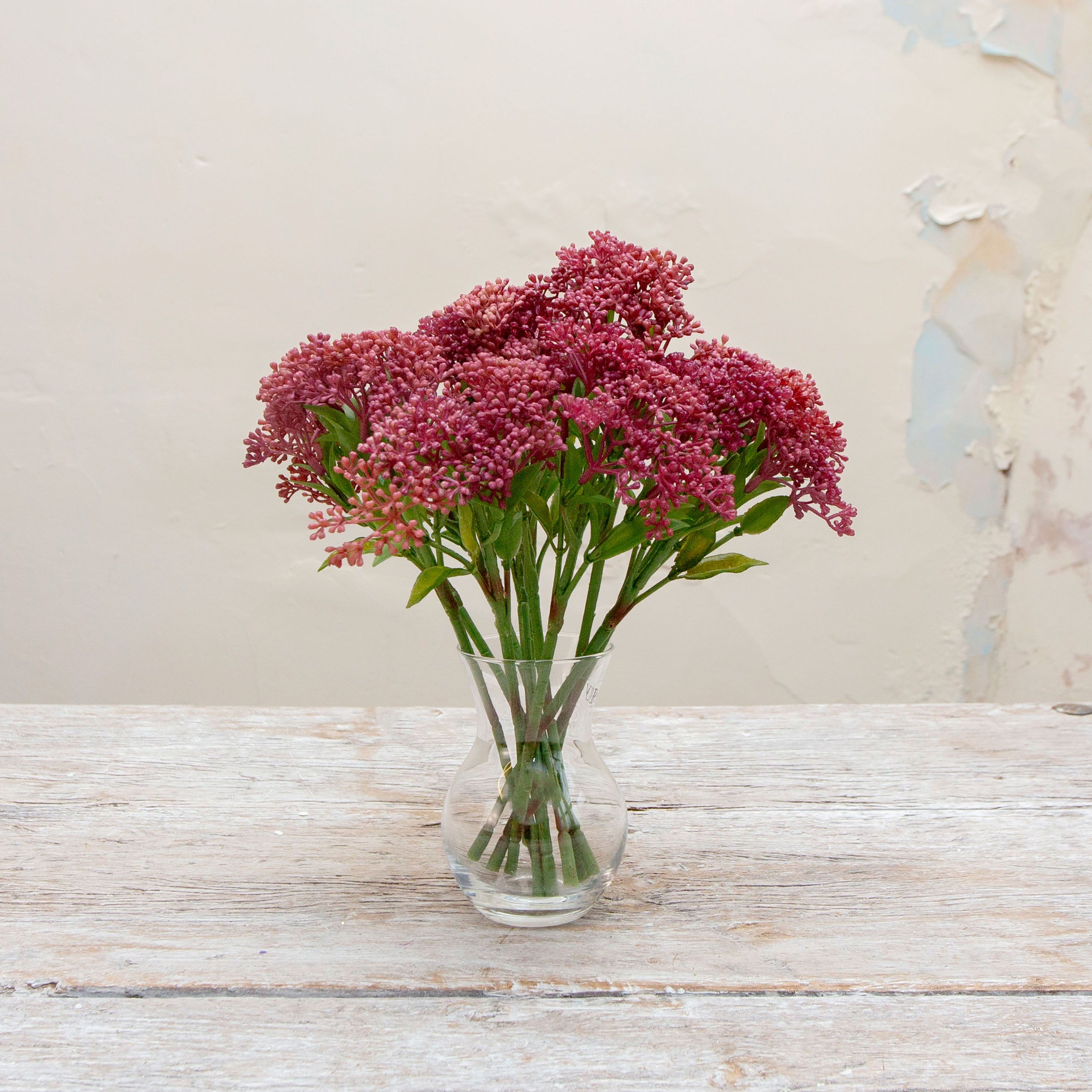 Artificial deep berry pink skimmia stems displayed together in a vase for styling purposes