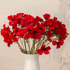 Close up of Artificial Red Dogwood Stems with vibrant red flowers and dark centres displayed in a white metal jug
