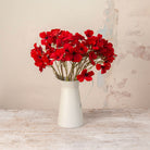 Artificial Red Dogwood Stems with vibrant red flowers and dark centres displayed in a white metal jug