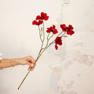 Hand holding Artificial Red Dogwood Stem with vibrant red flowers and dark centres